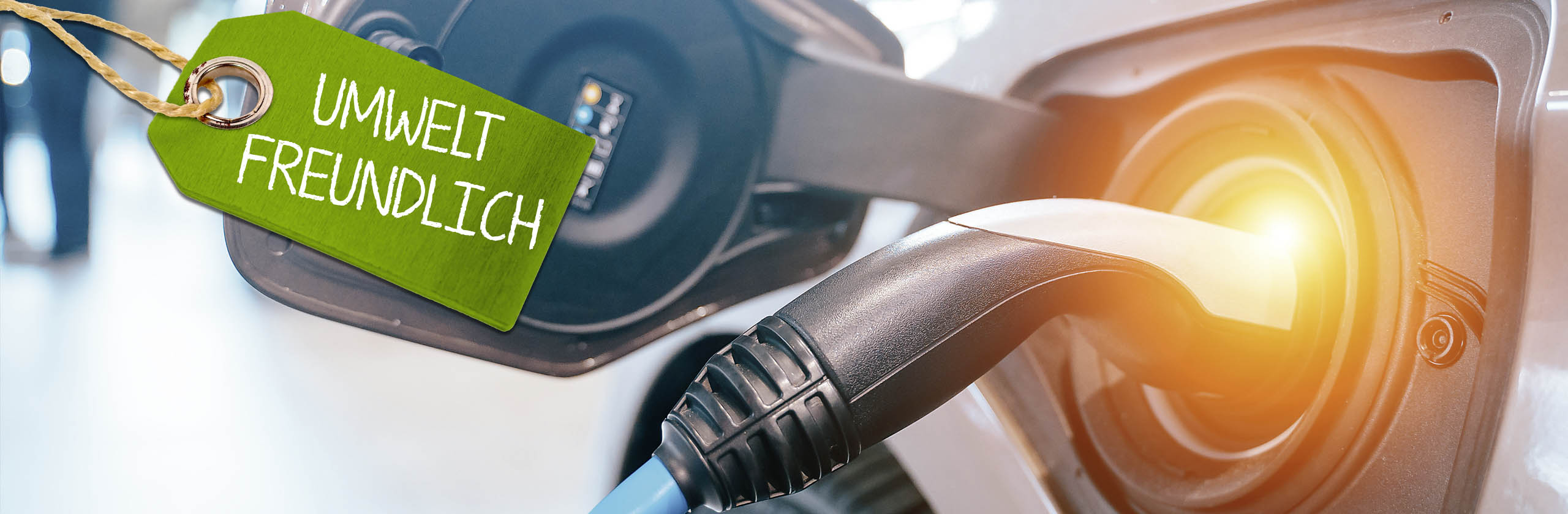 Kopfzeilenbild Elektromobilität, dekorativer Zweck - Das dekorative Bild zeigt ein Elektrofahrzeug beim Ladevorgang und ein plakatives Element mit der Aufschrift "Umweltfreundlich".